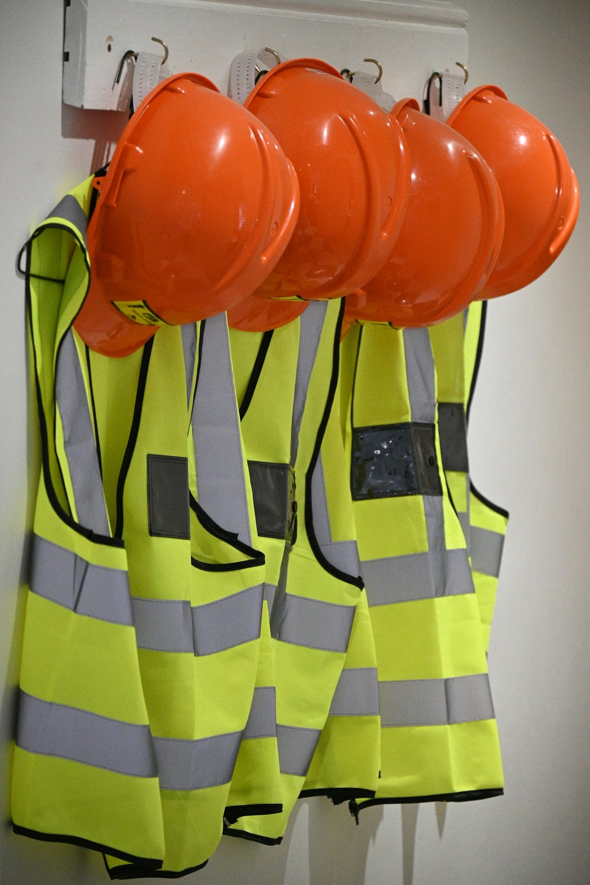 Orange hard hats and high-visibility safety vests hanging on a jobsite wall