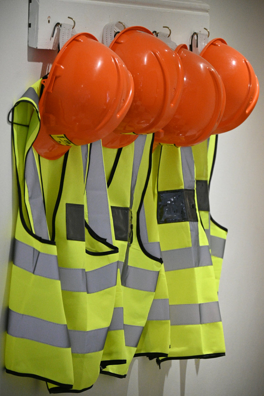 Orange hard hats and high-visibility safety vests hanging on a jobsite wall